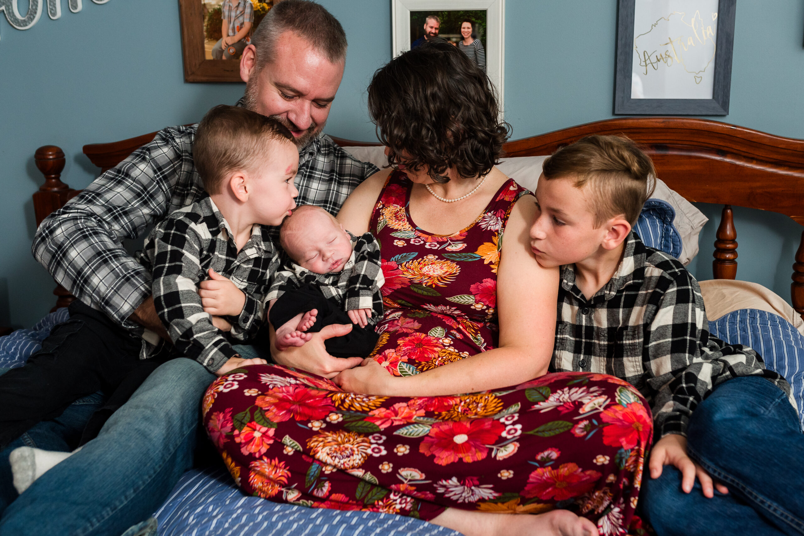 family of 5 sitting on bed, mom, dad and 3 boys with newborn baby