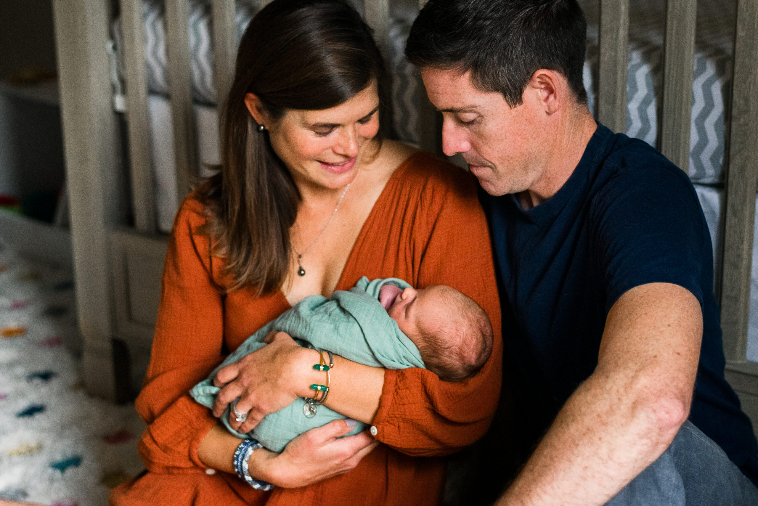 mom holding newborn with dad sitting next to her looking at baby