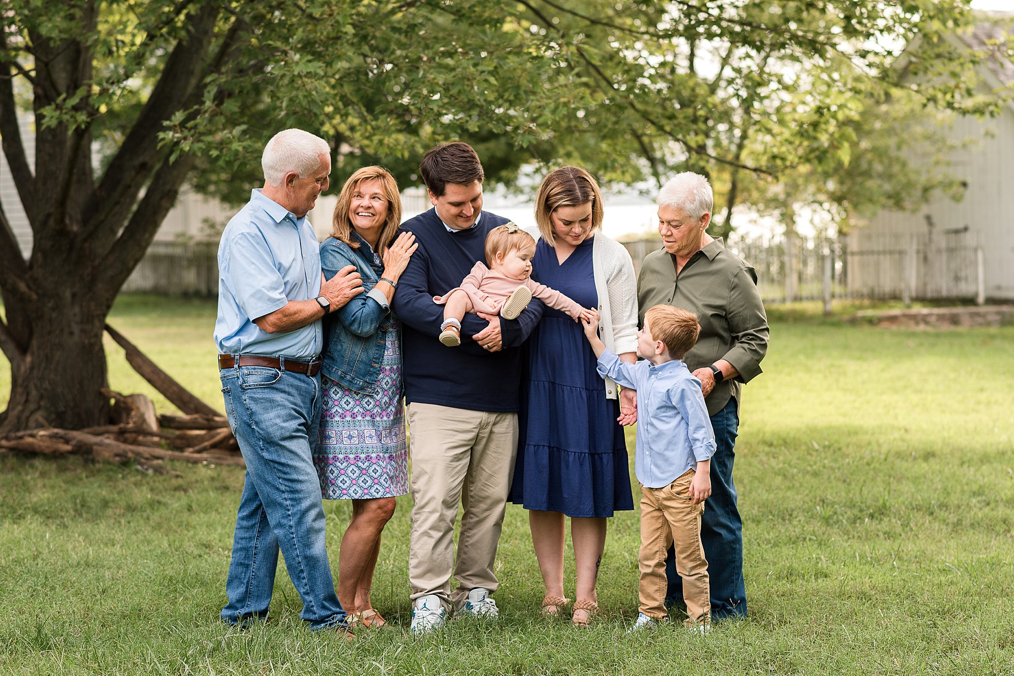 family of mom, dad, two kids and grandparents pose in field under tree