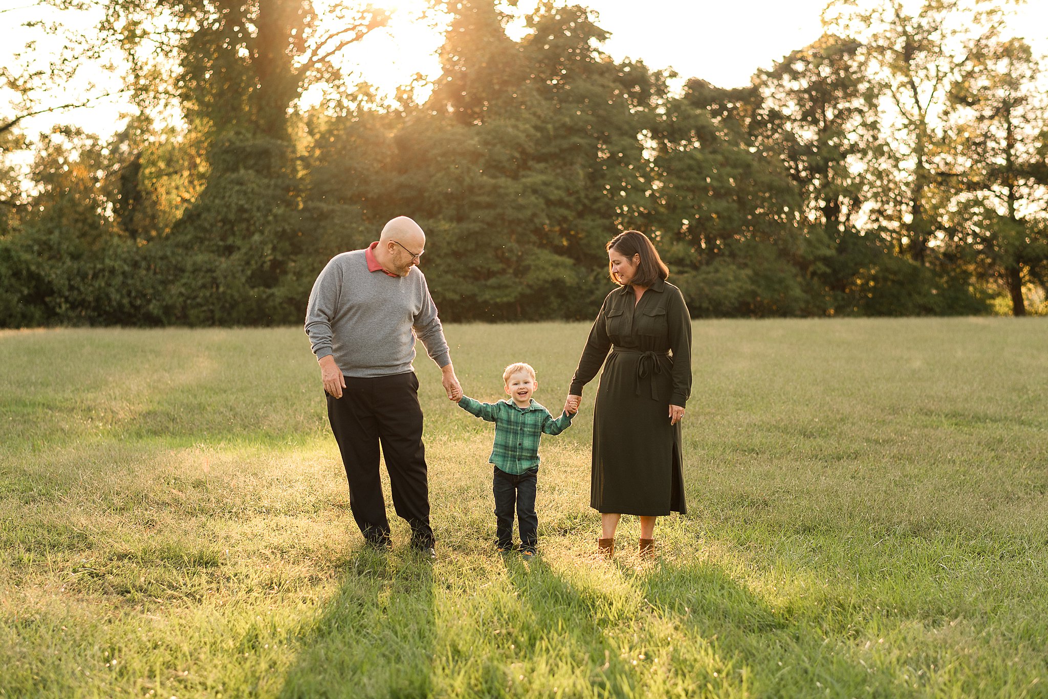 family of three, mom, dad and little boy, holding hands in a field